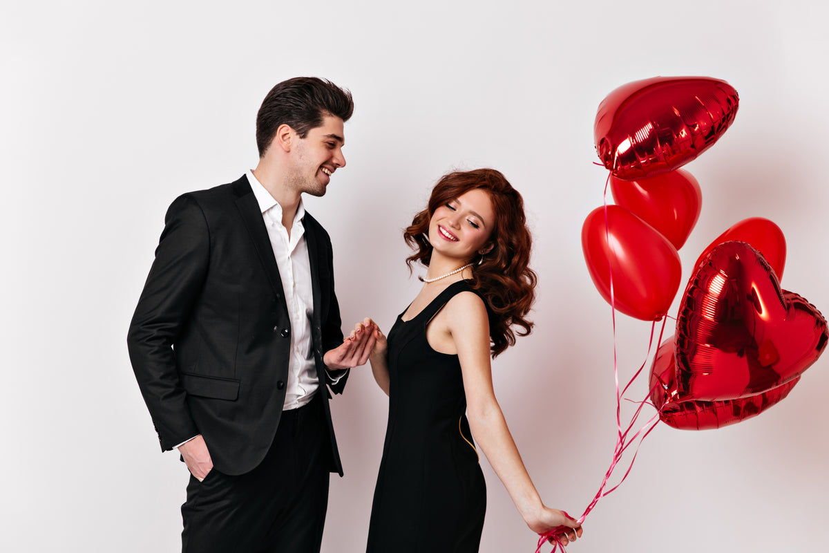 A couple celebrating Valentine's Day in elegant outfits with red heart-shaped balloons